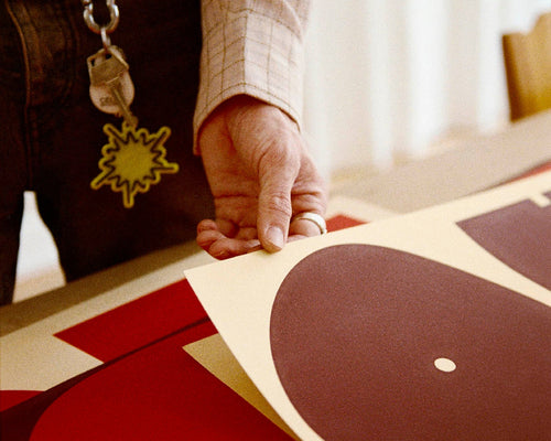Close up of hand holding edge of art print, feeling it with their thumb.