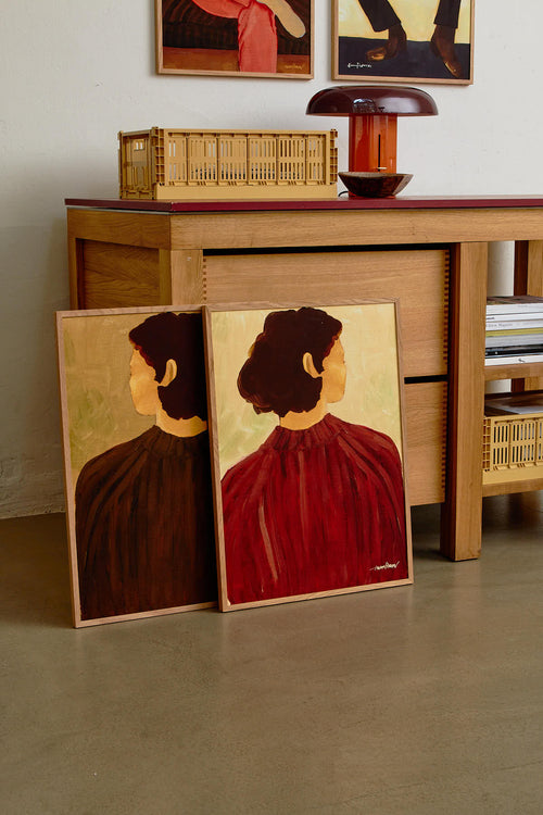 Two paintings of a woman in a red dress and black top on a wooden floor with a wooden cabinet in the background.