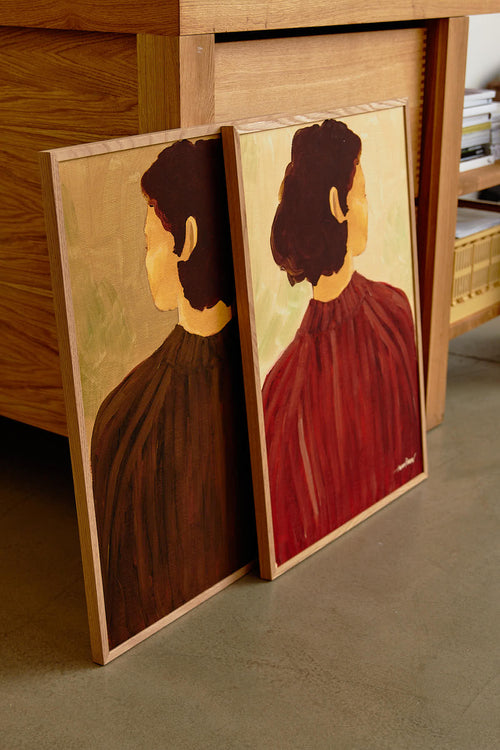 Two paintings of a woman with dark hair, one in brown and one in red, leaning against a wooden surface.