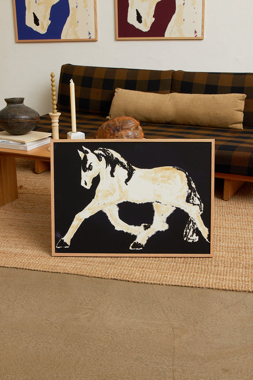 Art print with a stylized illustration of a horse in motion in light beige and black tones against a black background, with an intentionally blurred and painterly feel. Styled in a minimalist interior.