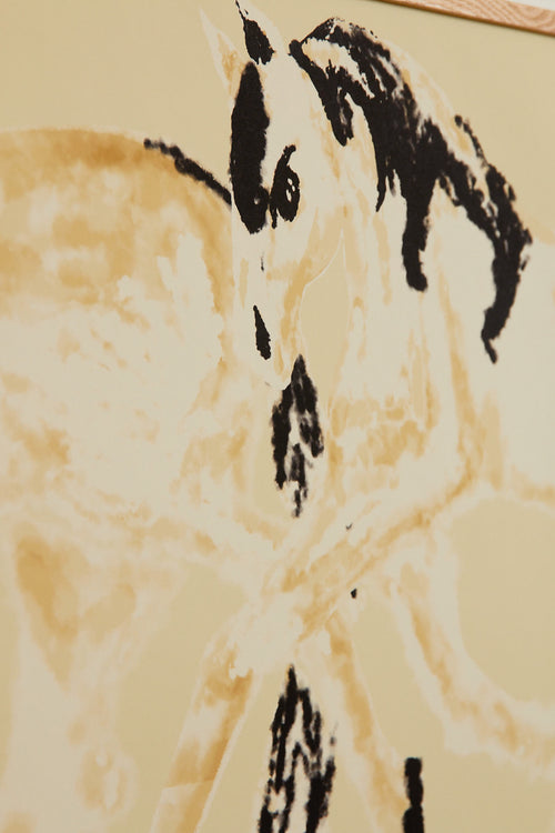 Art print with a stylized illustration of two mirrored horses in motion in light beige and black tones against a yellow-beige background, with an intentionally blurred and painterly feel. Styled in a minimalist interior.