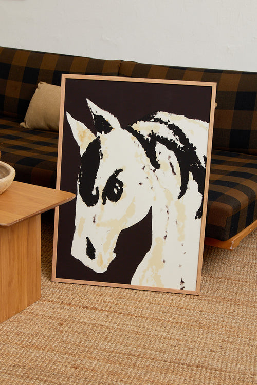 Art print with a stylized illustration of a horse head in light beige and black tones against a dark brown background, with an intentionally blurred and painterly feel. Styled in a minimalist interior.