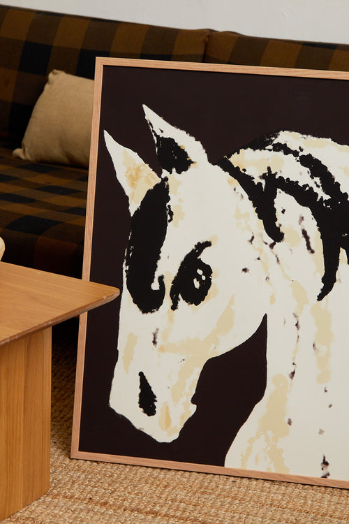 Art print with a stylized illustration of a horse head in light beige and black tones against a dark brown background, with an intentionally blurred and painterly feel. Styled in a minimalist interior.