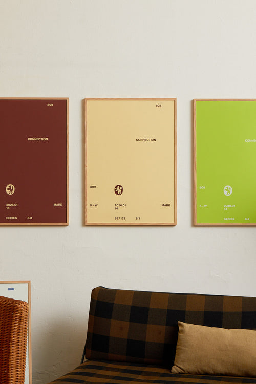 Art print with minimalist, small graphic text elements and a symbol motif in brown against a beige background. Styled in a minimalist interior.