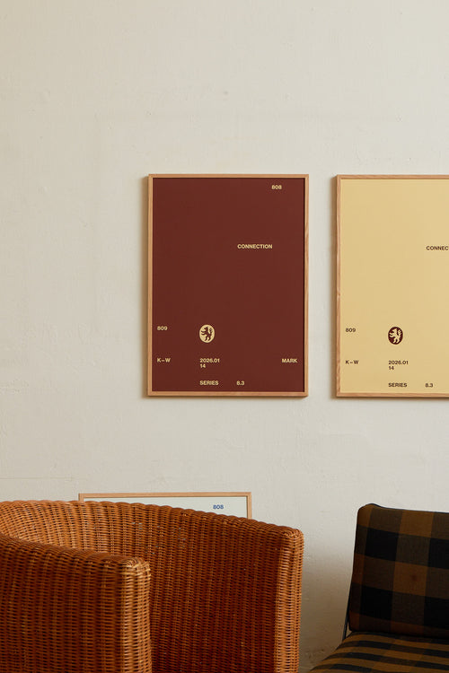 Art print with minimalist, small graphic text elements and a symbol motif in beige against a brown background. Styled in a minimalist interior.