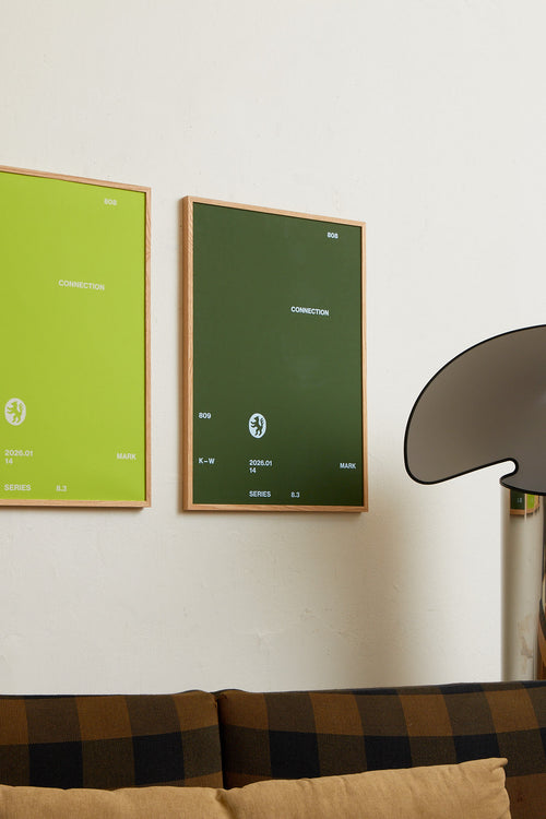 Art print with minimalist, small graphic text elements and a symbol motif in light blue against a moss green background. Styled in a minimalist interior.