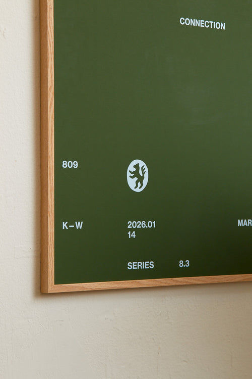 Art print with minimalist, small graphic text elements and a symbol motif in light blue against a moss green background. Styled in a minimalist interior.