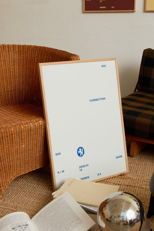 Art print with minimalist, small graphic text elements and a symbol motif in navy blue against a light blue background. Styled in a minimalist interior.