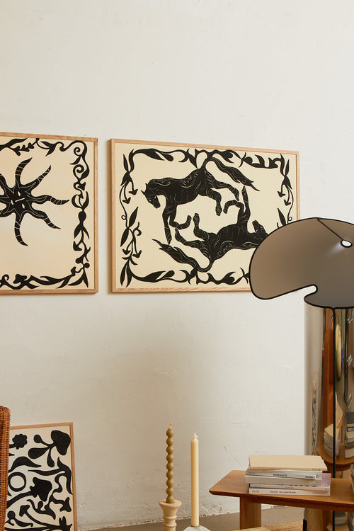 Art print with a minimalist illustration of black, organic, hand-drawn lines and silhouettes of horses against an off-white background. Styled in a minimalist interior.