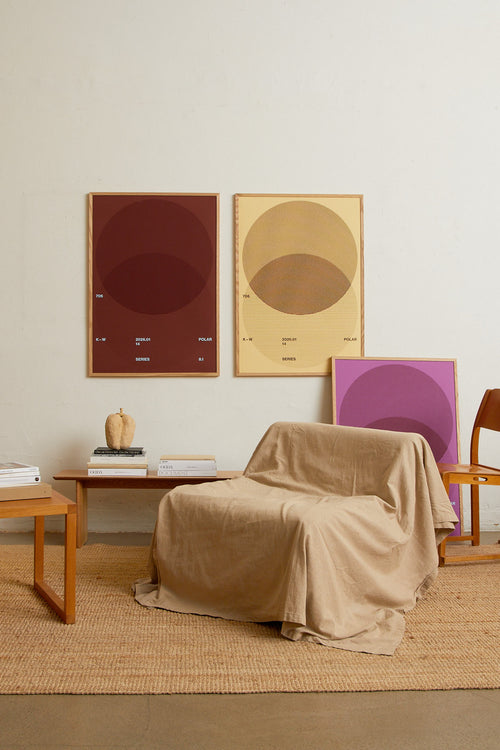 Art print with a graphic illustration of circular forms built from overlapping lines, complemented by small text elements, in brown, red, and beige RAL colors. Styled in a minimalist interior.