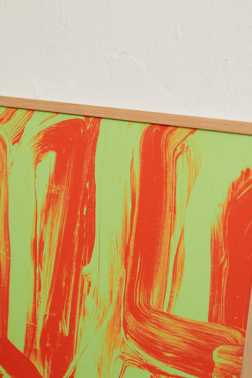 Art print featuring layered and sweeping brushstrokes in bright orange and green that create a sense of movement and tension across the surface. Styled in a minimalist interior.