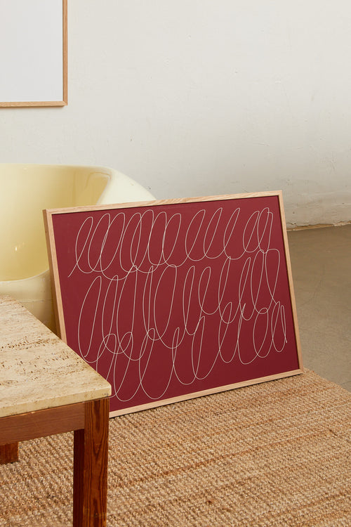 Art print with a graphic illustration of sweeping, continuous lines in a light tone against a red background, with a minimalist and abstract expression. Styled in a minimalist interior.
