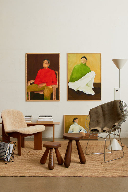 Art print featuring a painting of a person sitting on the ground, with a green sweater, light checkered bottoms, and dark loafers against a neutral background in dark brown and ochre. Styled in a minimalist interior.