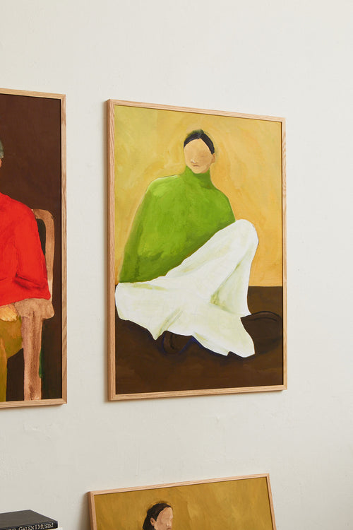 Art print featuring a painting of a person sitting on the ground, with a green sweater, light checkered bottoms, and dark loafers against a neutral background in dark brown and ochre. Styled in a minimalist interior.