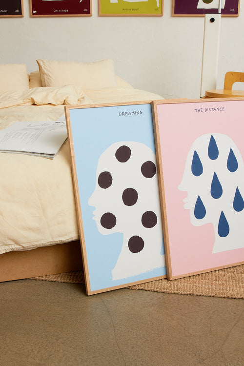 Framed “Thinking” print leaning against a wall beside a bed in a softly styled bedroom