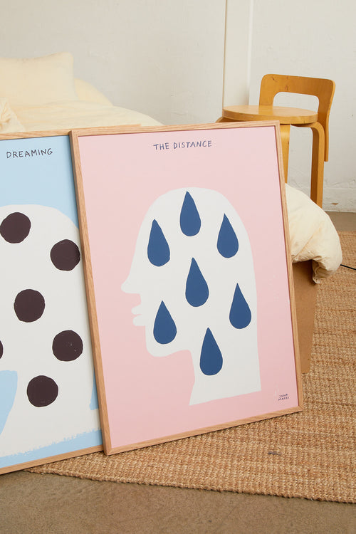 Art print featuring a silhouette of a head in profile with drops and the handwritten note “The Distance”. Styled in a minimalist interior.