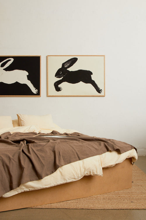 Art print with a stylized illustration of a hare in a dark tone against an off-white background, with a minimalist and graphic expression. Styled in a minimalist interior.