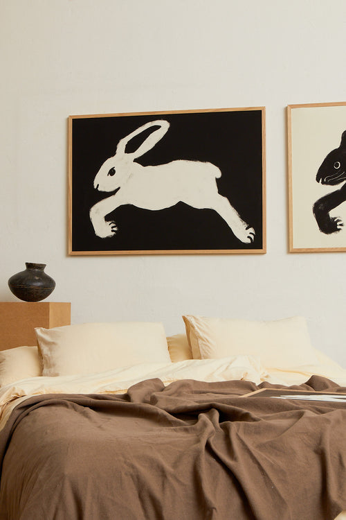 Art print with a stylized illustration of a hare in a light tone against a black background, with a minimalist and graphic expression. Styled in a minimalist interior.
