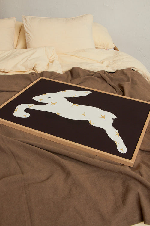 Art print with a stylized illustration of a hare in a light tone with stars against a dark brown background, with a minimalist and graphic expression. Styled in a minimalist interior.