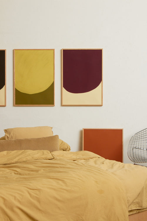 Art print with a minimalist illustration of a large, rounded color field in a yellow tone against a green background. Styled in a minimalist interior.