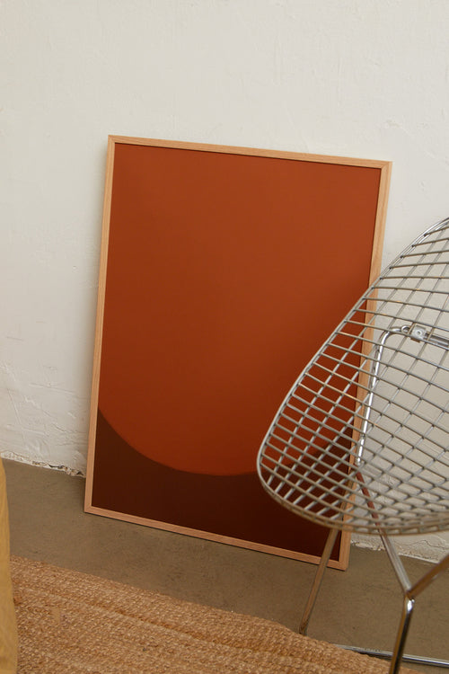 Art print with a minimalist illustration of a large, rounded color field in an orange tone against a brown-orange background. Styled in a minimalist interior.
