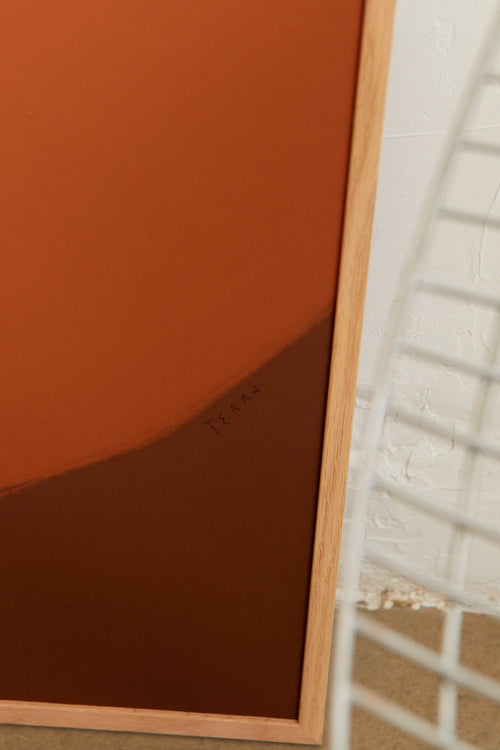 Art print with a minimalist illustration of a large, rounded color field in an orange tone against a brown-orange background. Styled in a minimalist interior.