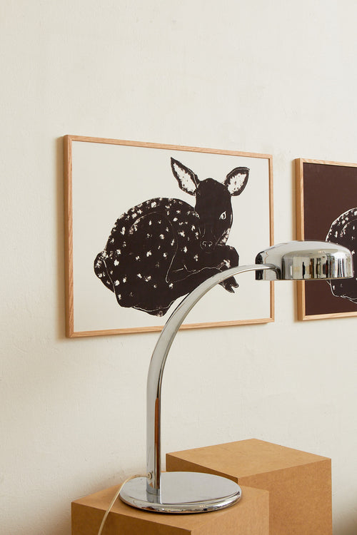 Art print with a stylized illustration of a lying deer in a dark tone against a, with a minimalist and graphic expression. Styled in a minimalist interior.