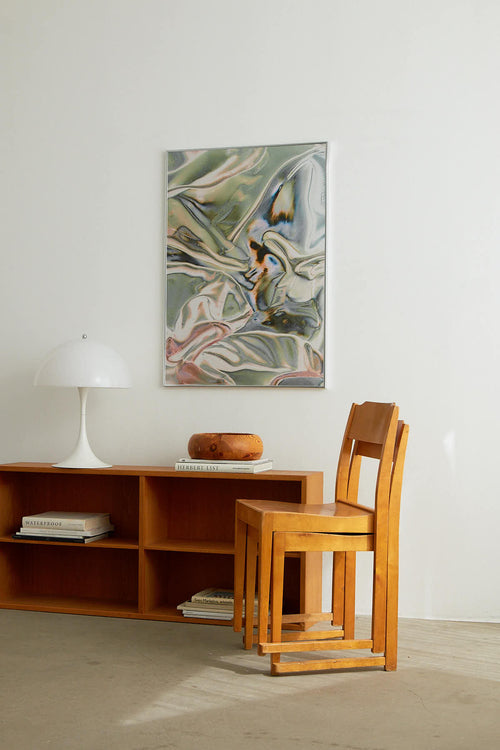 Wooden chair and table set against a white wall with abstract art above.