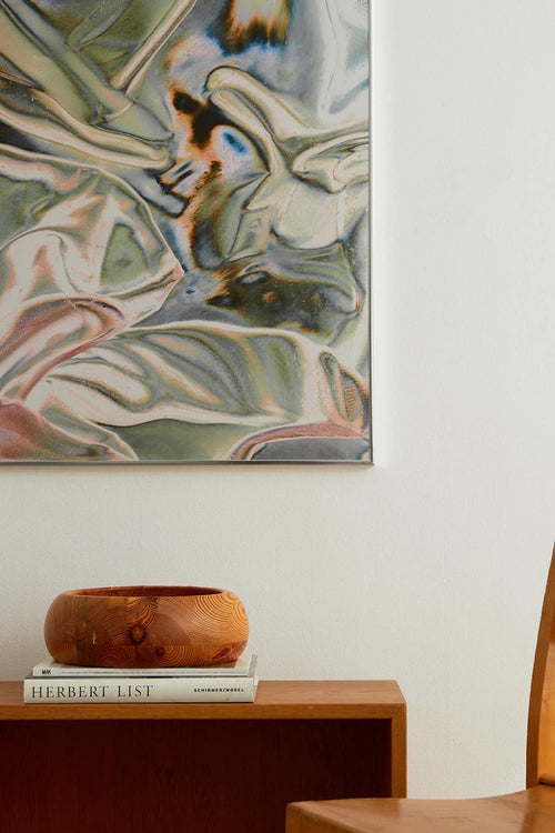 Abstract painting on a wall with a wooden bowl and books below