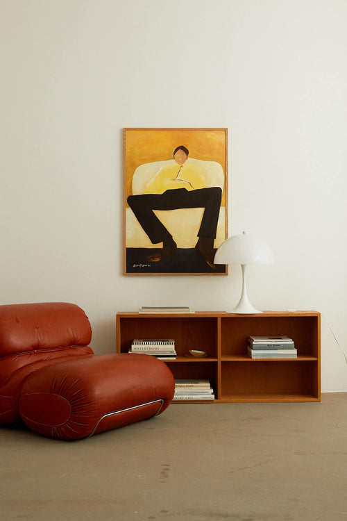 Living room with a red leather chair, wooden shelf, and framed artwork on the wall.