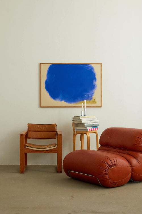 Modern living room with a red sofa, brown chair, and abstract blue painting on the wall.