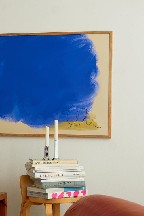 Stack of books on a small table with a colorful abstract painting in the background.