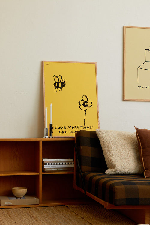 Yellow framed poster with a bee design on a wall above a wooden shelf and sofa.