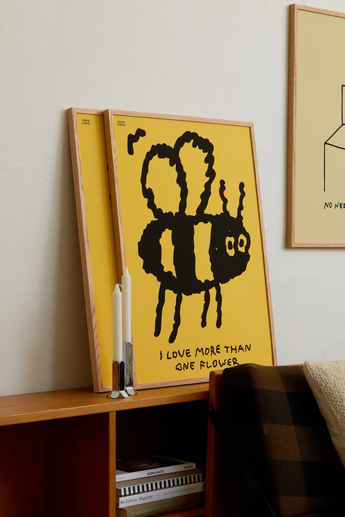 Yellow poster with a black bee illustration and text on a shelf against a white wall.