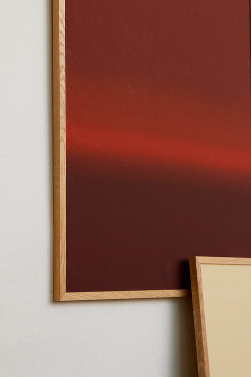 Framed abstract artwork with a gradient red background on a white wall.