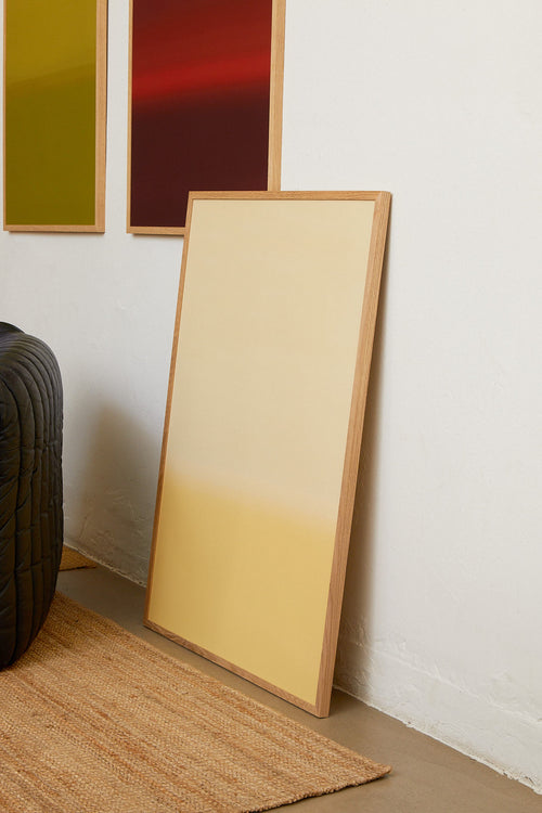 Floor mirror with wooden frame leaning against a white wall.