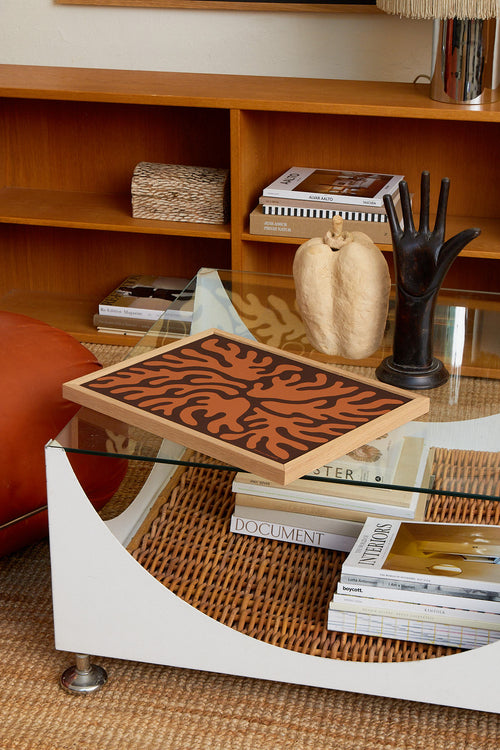 Decorative tray with leaf pattern on a glass coffee table with books and decor items.