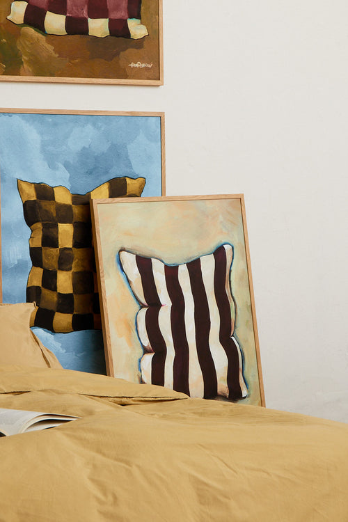Bed with mustard-colored bedding, striped pillow, and framed abstract art on a white wall.