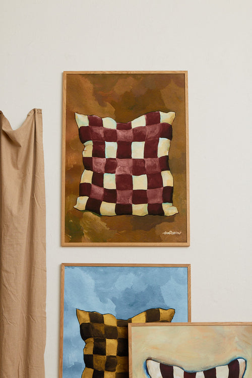 Framed artwork of a checkered pillow on a wall with other framed pieces.