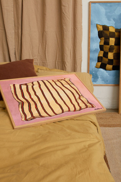 Bed with striped pillow on a pink blanket, beige curtains, and abstract painting in the background.