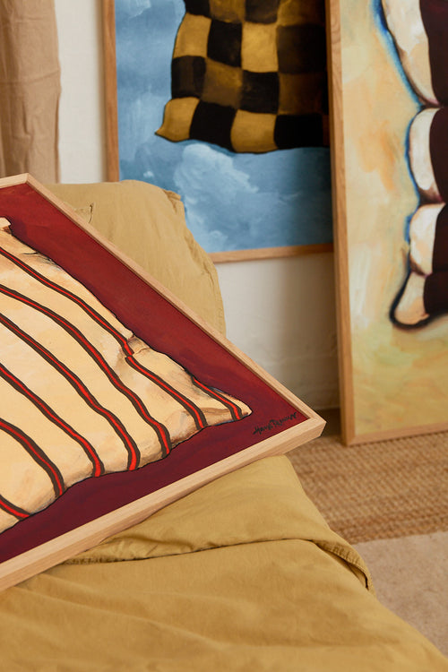 Decorative pillow with striped pattern on a bed in a room with abstract art on the wall.