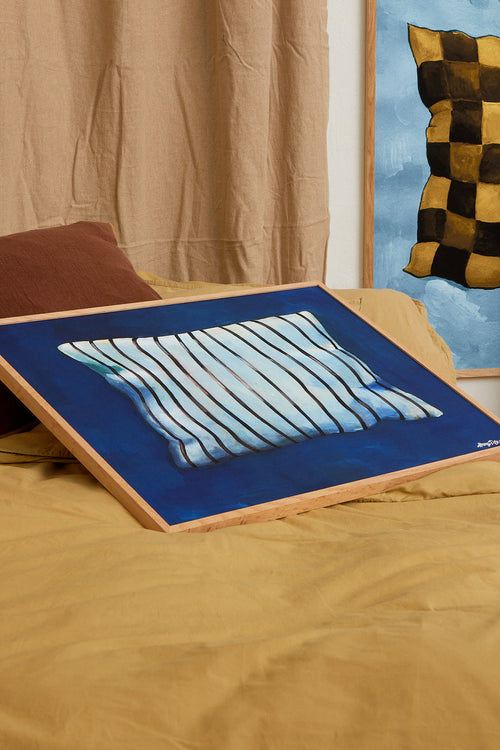 Blue and white striped pillow on a wooden board against a beige curtain and colorful wall.