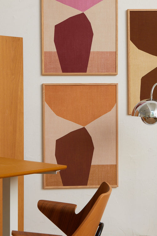 Abstract art pieces on a wall with a wooden table and chair in the foreground.