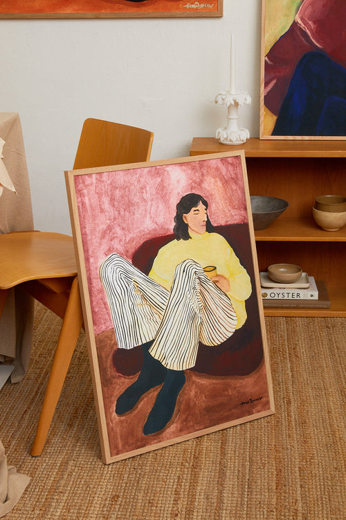 Framed artwork of a woman in a yellow sweater on a wooden floor.