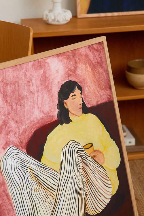 Artistic depiction of a person in a yellow garment with a pink background, framed in a wooden frame.