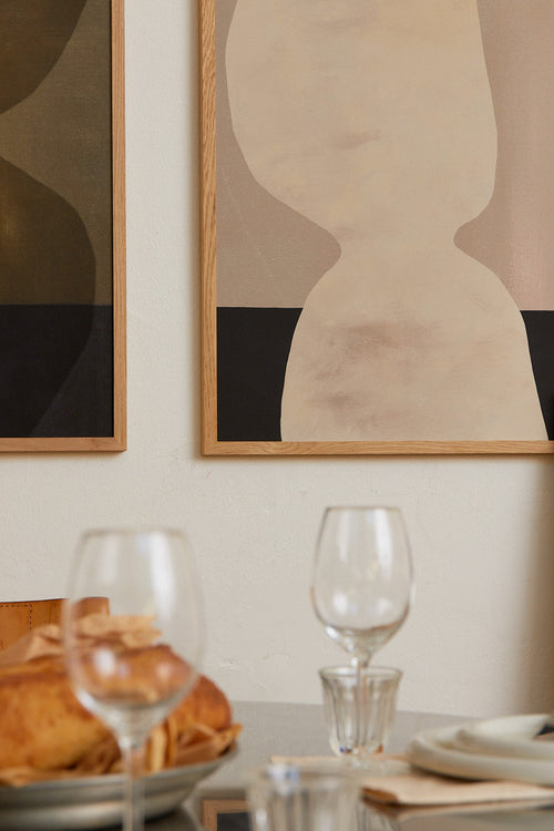 Dining table setting with wine glasses and plates against a wall with abstract art.