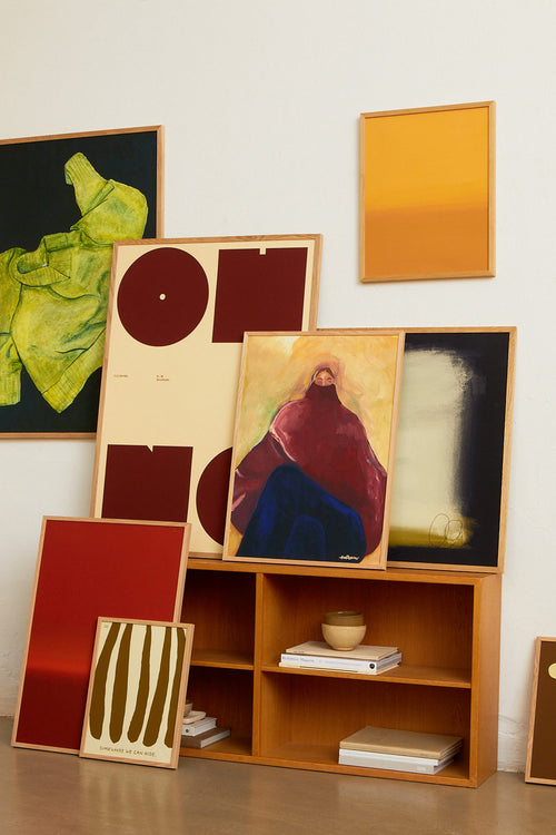 Collection of abstract artworks on a wooden shelf against a white wall.