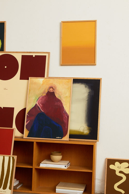 Wooden bookshelf with framed artworks on a white wall