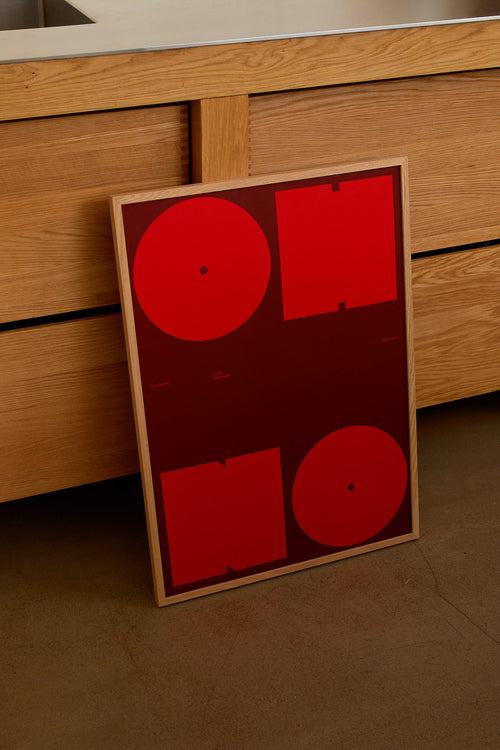 Framed abstract artwork with red shapes on a wooden surface