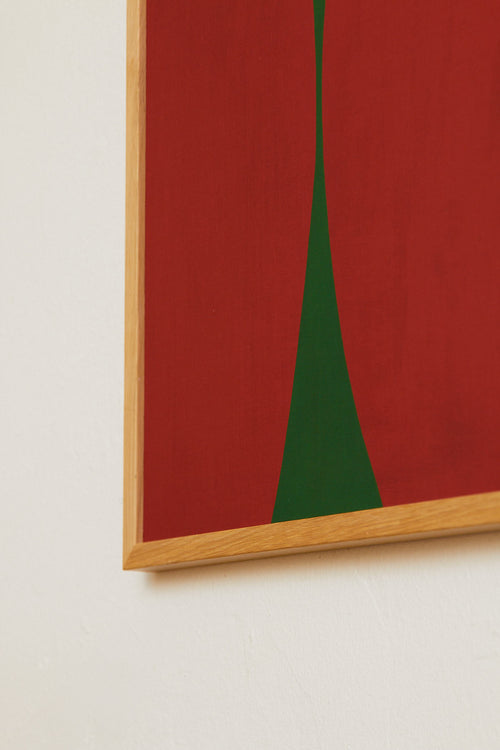Framed artwork with a red background and green triangle on a light beige wall.